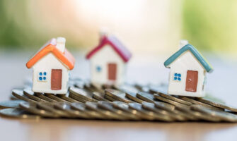 Finance & Investment Concept - A Wooden Kit of The Houses Placed Behind Coins.